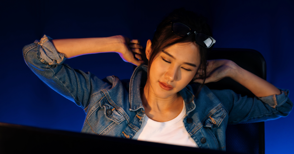 A gamer stretching quietly in a dimly lit room, with their setup powered down and a soft bedside glow nearby. Gamer recovery is vital to gaming performance.