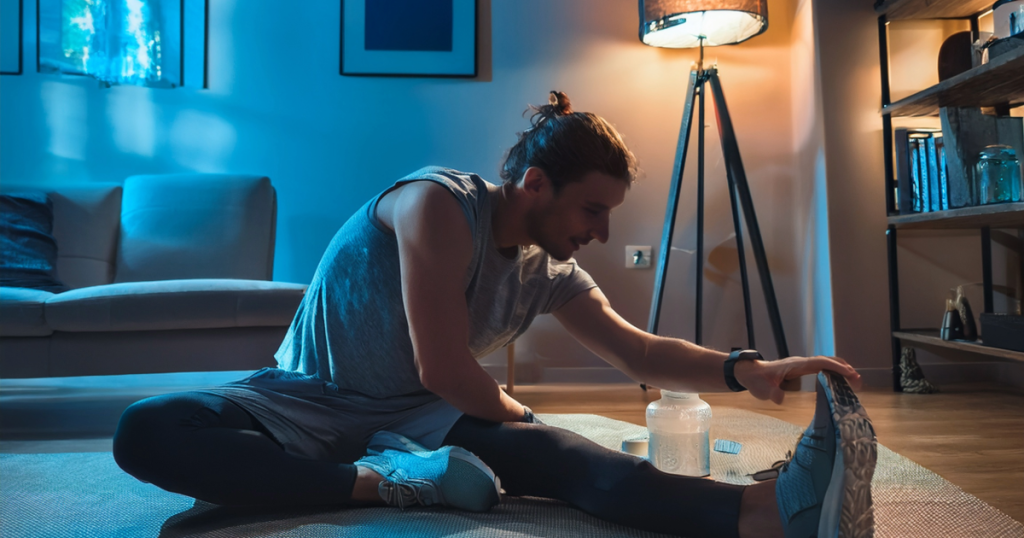 Someone stretching lightly in a calm room with visible wearables or a recovery drink nearby, signaling preparation for rest as part of a cooldown plan